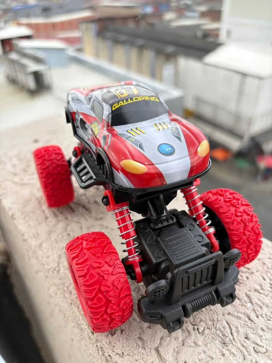 Carro todoterreno a escala rojo y gris con suspensión alta y llantas grandes texturizadas, sobre superficie de concreto.