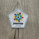 Parche termoadhesivo oficial DIMAYOR pentagonal sobre superficie de madera, con diseño colorido de balón y polígonos alrededor.