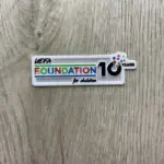 Parche termoadhesivo blanco rectangular de UEFA Foundation for Children 10 Years con letras coloridas, sobre superficie de madera.