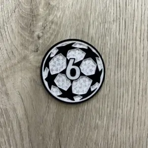 Parche termoadhesivo circular con diseño de balón de estrellas blancas y negras y el número 6 en el centro, sobre fondo de madera.