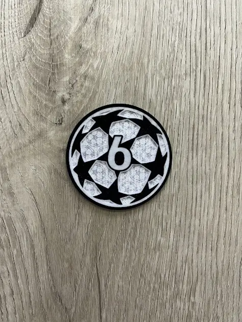 Parche termoadhesivo circular con diseño de balón de estrellas blancas y negras y el número 6 en el centro, sobre fondo de madera.