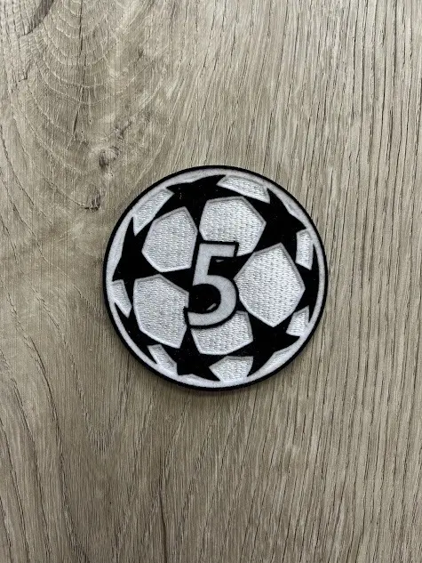 Parche termoadhesivo redondo con el número 5 blanco sobre diseño de balón de fútbol en blanco y negro, bordado sobre fondo de madera.