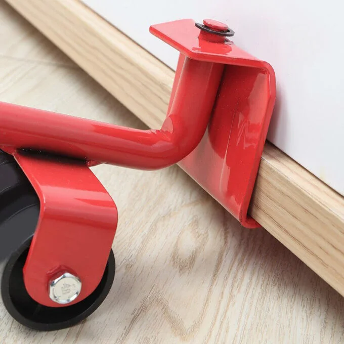 Elevador de muebles rojo de metal con rueda pivotante y gancho ajustable, apoyado sobre la base de un mueble de madera.