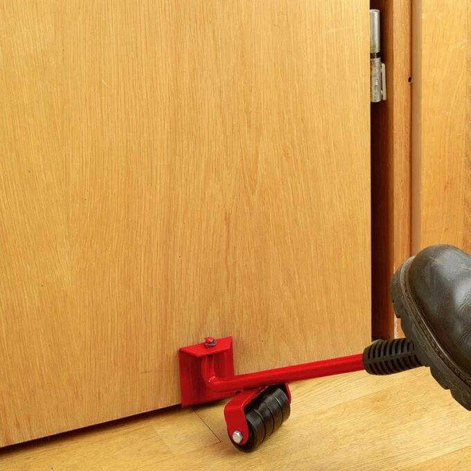 Palanca elevadora roja con rodillos negros para levantar una puerta de madera con el pie, facilitando su instalación.