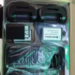 Caja abierta de radio intercomunicador portátil C1, incluye dos radios negros envueltos en plástico, dos bases de carga, dos baterías Motorola, adaptador de pared y cable USB.