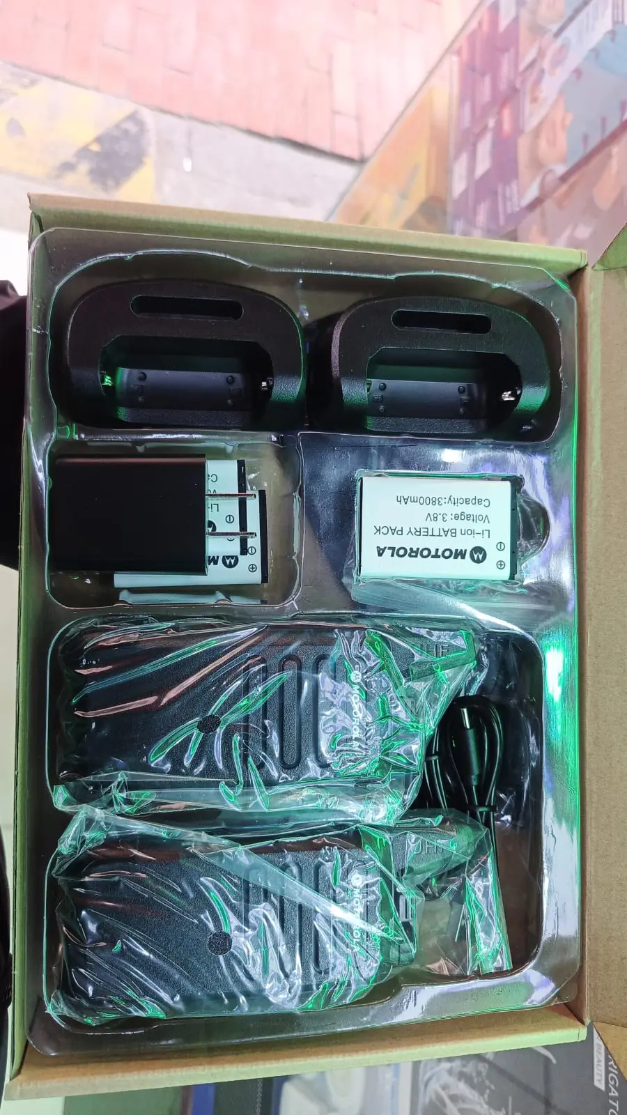 Caja abierta de radio intercomunicador portátil C1, incluye dos radios negros envueltos en plástico, dos bases de carga, dos baterías Motorola, adaptador de pared y cable USB.