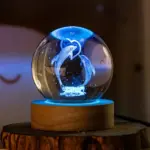 Esfera de cristal 3D con grabado de delfines y corazón, iluminada con luz azul sobre base de madera para decoración ambiental.