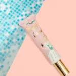 Base Queen Face Tint en tubo rosa con de princesa y tapa dorada, sobre fondo dividido de mosaico azul y rosa.