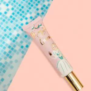 Base Queen Face Tint en tubo rosa con de princesa y tapa dorada, sobre fondo dividido de mosaico azul y rosa.