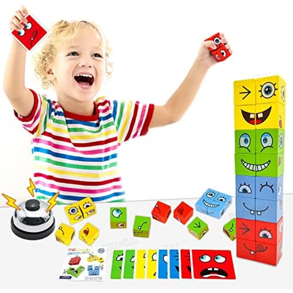 Niño sonriente juega con cubos de madera coloridos de expresiones faciales, tarjetas de emociones y timbre de mesa sobre superficie blanca.