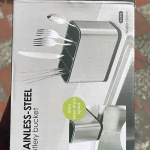 Caja de organizador de cubiertos en acero inoxidable con divisiones, espátula de drenaje y dimensiones de 180x86x130mm sobre fondo gris.