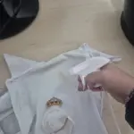 Mano usando enhebrador automático blanco de plástico sobre tela, demostrando su facilidad para insertar el hilo.