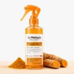 Spray exfoliante corporal y de pies Dr Melaxin con ácido kójico, cúrcuma y niacinamida, en botella transparente de 200 ml con atomizador naranja, junto a cúrcuma en polvo y raíces de cúrcuma frescas.