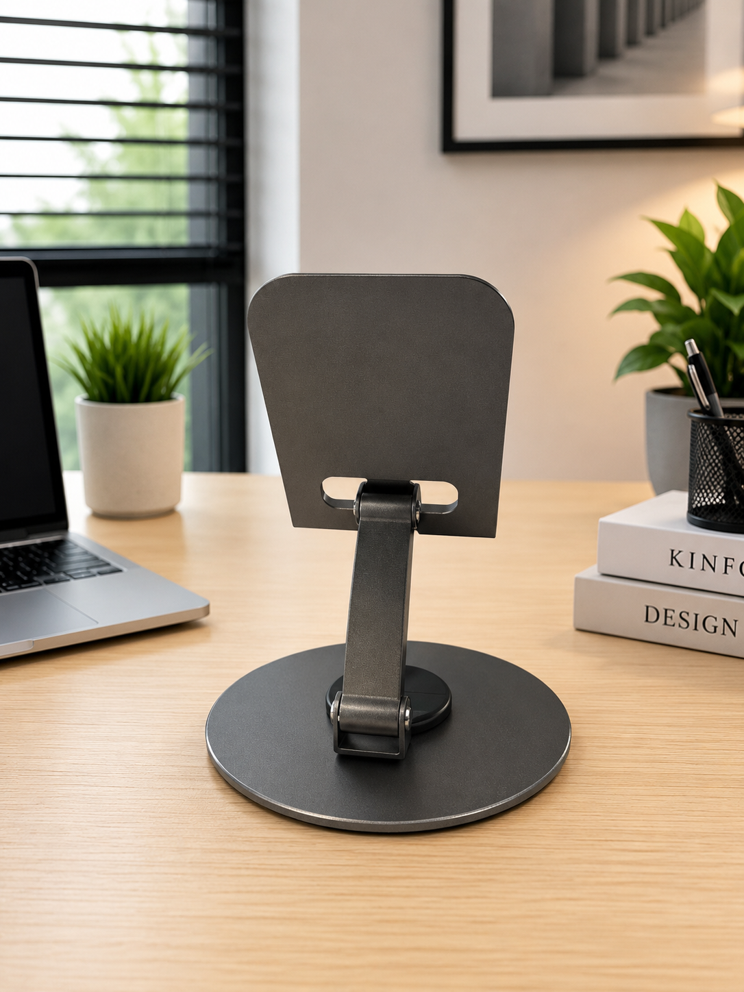 Soporte de escritorio ajustable gris para celular y smartphone con base circular y brazo articulado metálico sobre mesa de madera.