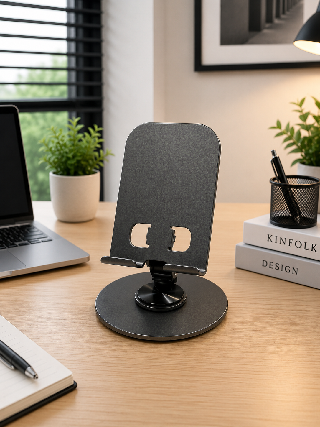Soporte de escritorio ajustable negro mate para celular con base redonda y gancho de apoyo sobre mesa de madera.