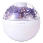 Humidificador esférico blanco con cúpula transparente que contiene flores moradas y rosadas, con luz ambiental suave.