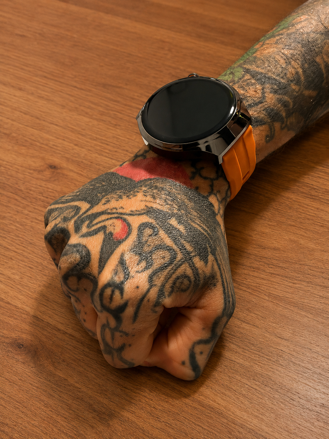 Reloj inteligente Vortexx Smart-Active negro con esfera redonda y correa naranja de silicona, colocado sobre una muñeca tatuada.