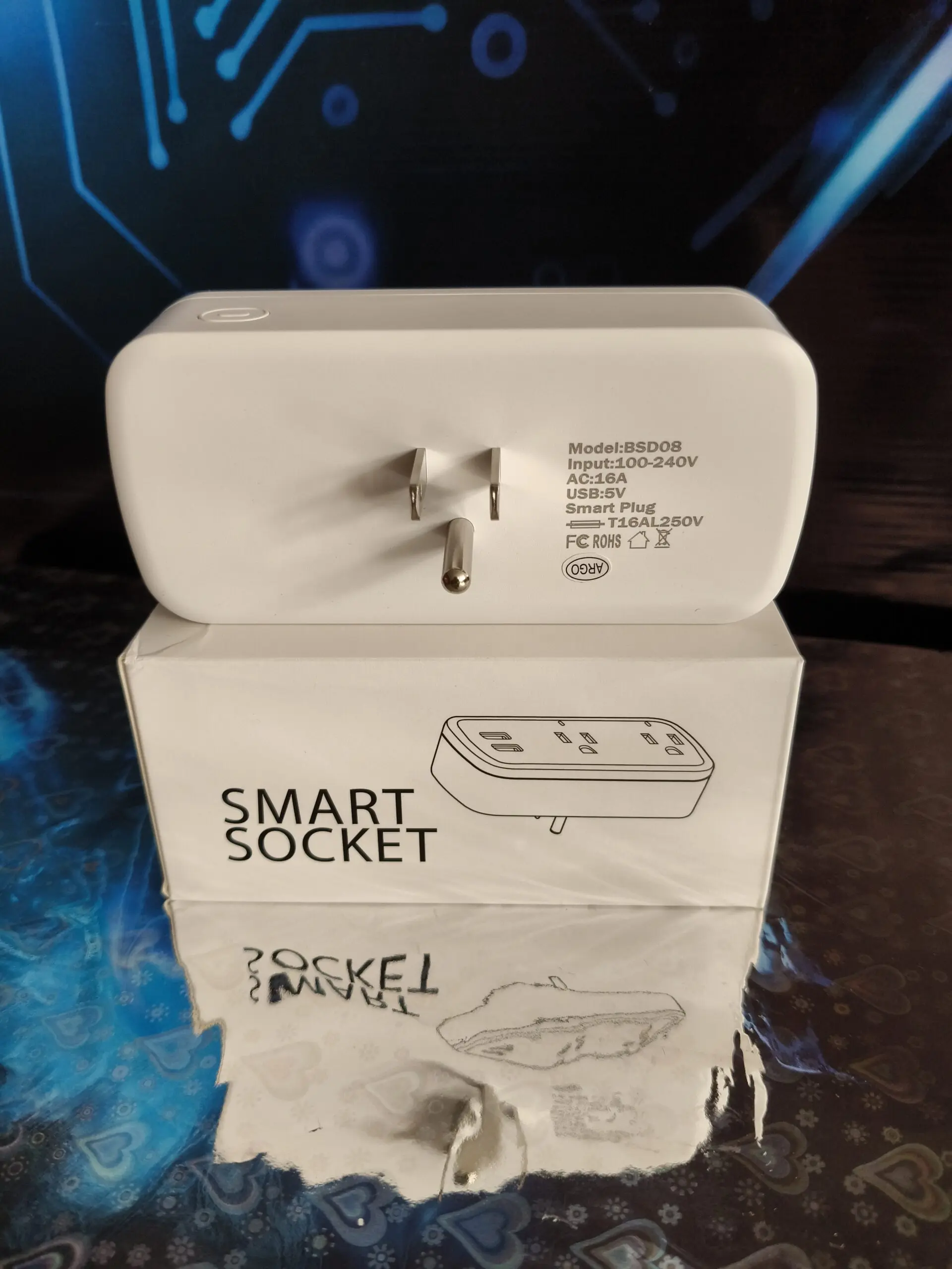 Tomacorriente inteligente WiFi blanco con dos tomas y USB, mostrado de espaldas sobre su caja de empaque con fondo de circuitos tecnológicos.