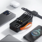 Power bank negro de carga rápida con pantalla LED digital, cuatro cables integrados, correa naranja y accesorios cargándose.