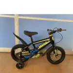 Bicicleta infantil negra Rin 12 con diseño Oracle en amarillo y azul, guardafangos, asiento negro ajustable y ruedas estabilizadoras.