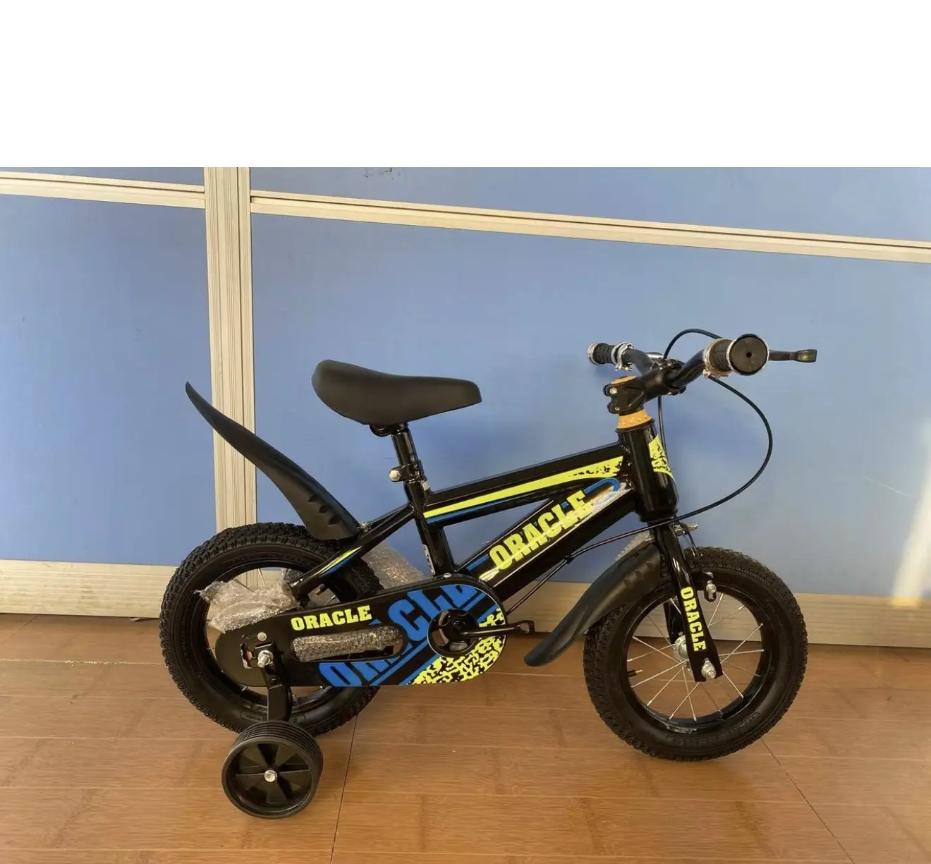 Bicicleta infantil negra Rin 12 con diseño Oracle en amarillo y azul, guardafangos, asiento negro ajustable y ruedas estabilizadoras.