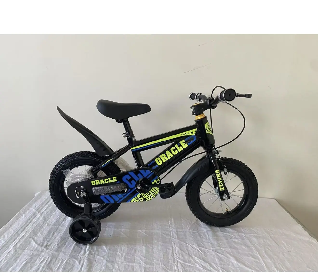 Bicicleta infantil negra Rin 12 con detalles amarillos y azules, guardafangos, pedales y ruedas estabilizadoras, sobre superficie blanca.
