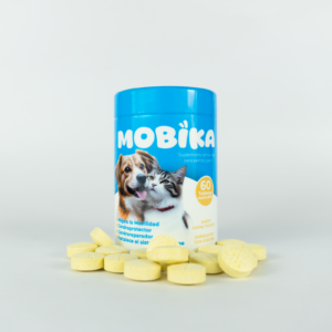 Frasco azul de suplemento articular Mobika para perros y gatos con tabletas amarillas esparcidas al frente sobre fondo blanco.