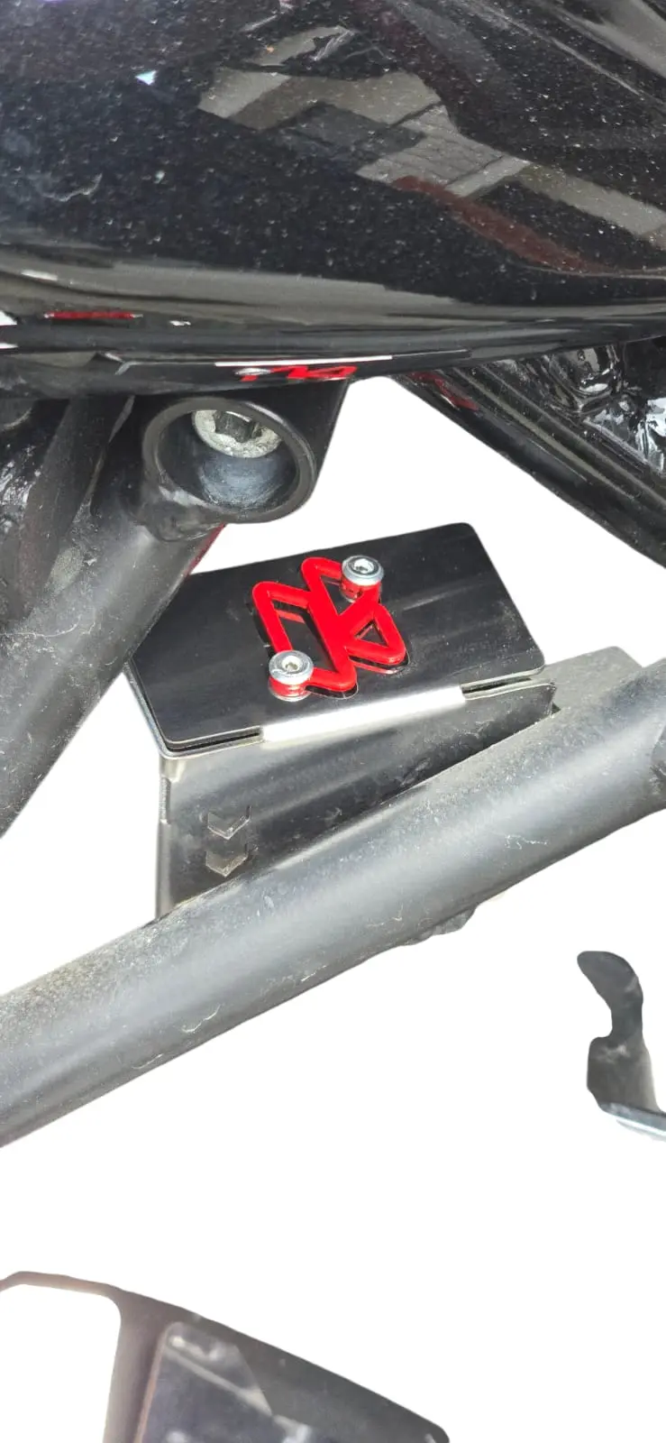 Protector de bomba de freno negra para Hunk 160R con detalle decorativo rojo, instalado sobre el chasis de la motocicleta.