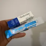 Mano sosteniendo caja blanca y azul de Bodywise y sobre azul de Citrato de Magnesio, combo de tratamiento capilar y suplemento.
