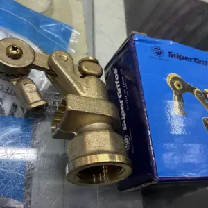 Válvula para tanque en bronce con diseño articulado y acabado metálico dorado, junto a su caja azul de la marca Super Grifos.