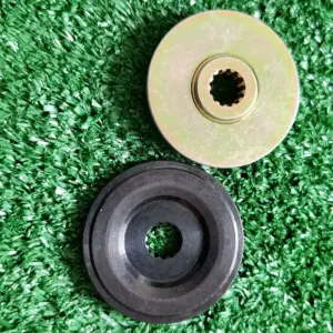 Placa de transmisión para guadaña con disco metálico dorado estriado y pieza circular negra sobre fondo de césped artificial.