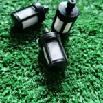 Tres filtros de combustible negros para motosierras Stihl MS381 y MS382, con cuerpo plástico y malla filtrante blanca, dispuestos sobre césped artificial.