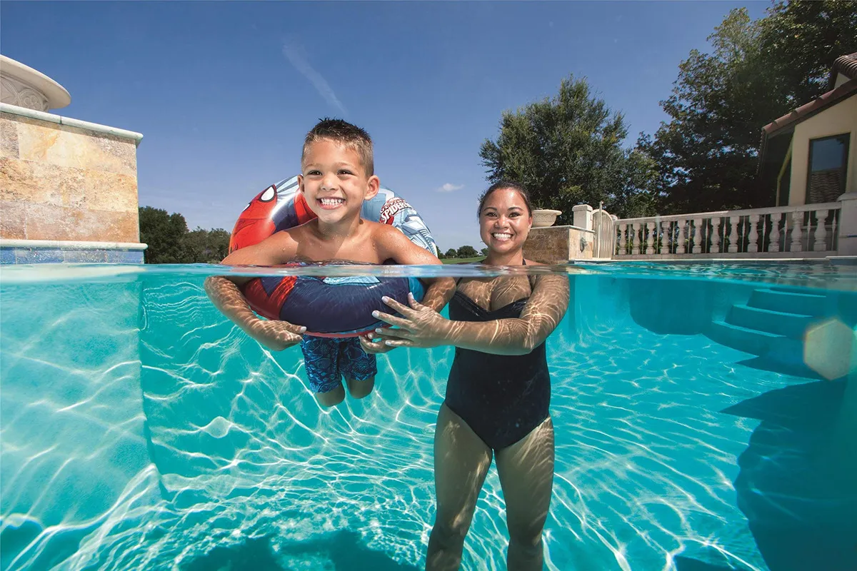 Flotador inflable de Spiderman rojo y azul usado por un niño en una piscina, toma de ángulo dividido entre la superficie y el agua cristalina.