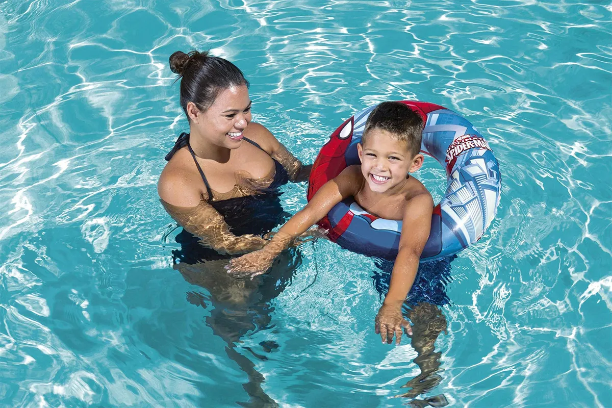 Flotador inflable azul y rojo de Spiderman para niños de 22 pulgadas, usado en piscina por un niño sonriente con supervisión.