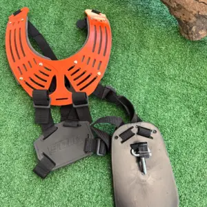 Arnés profesional STIHL para desbrozadora con soporte de pecho naranja ventilado, correas negras y placas de soporte gris sobre césped sintético.