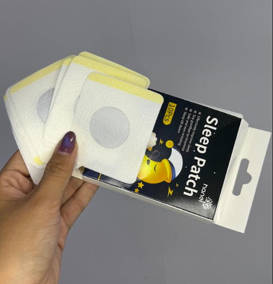 Mano sosteniendo caja de Sleep Patch con diez parches blancos cuadrados con centro circular gris y diseño de luna durmiendo