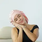 Gorro de satín rosado pastel con diseño fruncido, usado por mujer descansando para proteger el cabello rizado.