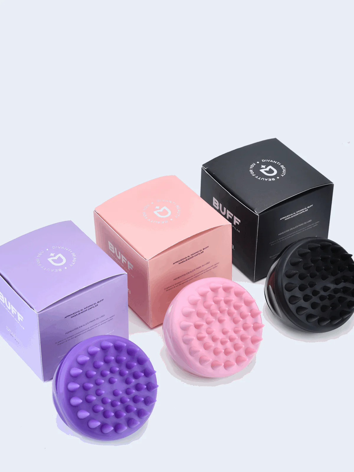 Tres cepillos masajeadores de cuero cabelludo con cerdas de silicona en colores morado, rosado y negro, cada uno junto a su caja de empaque correspondiente.
