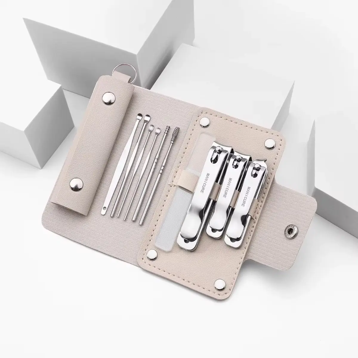 Estuche organizador de manicura compacto beige abierto, con diez piezas de acero inoxidable organizadas, incluyendo tres cortaúñas, pinzas y herramientas de precisión.