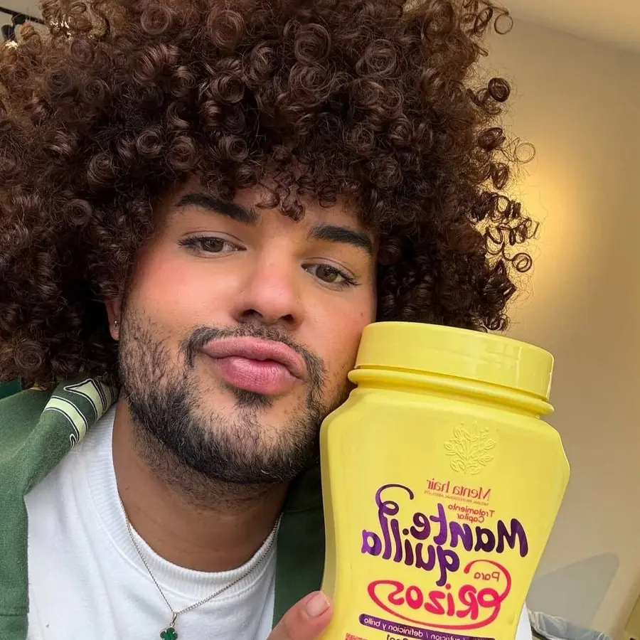 Hombre con cabello rizado castaño sostiene un pote amarillo de mantequilla para rizos de un litro.