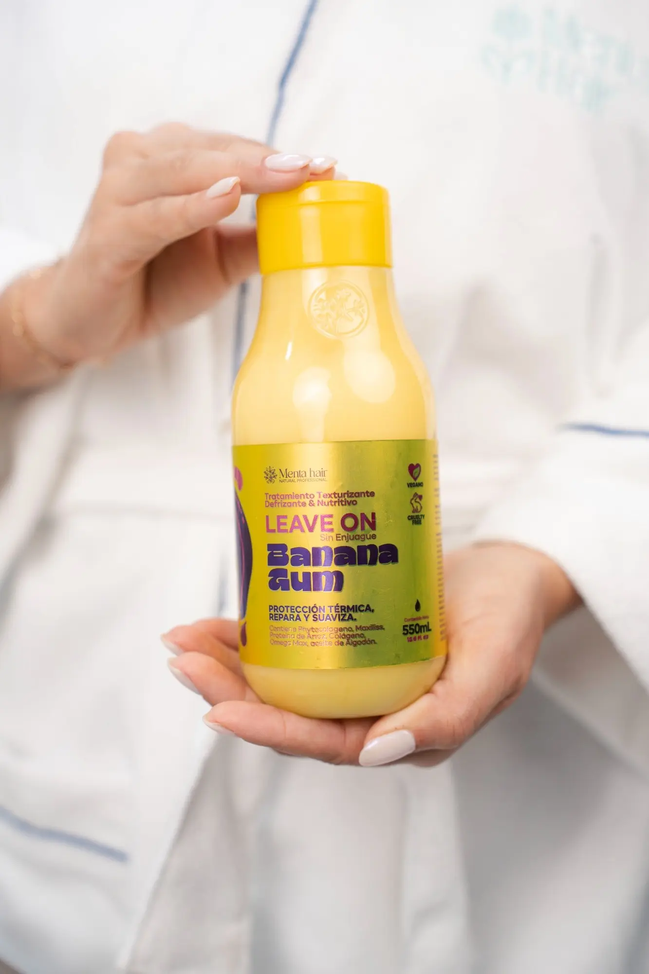 Frasco amarillo de crema para peinar Banana Gum de 550 ml sostenido con ambas manos, ideal para proteger del calor y controlar el frizz.
