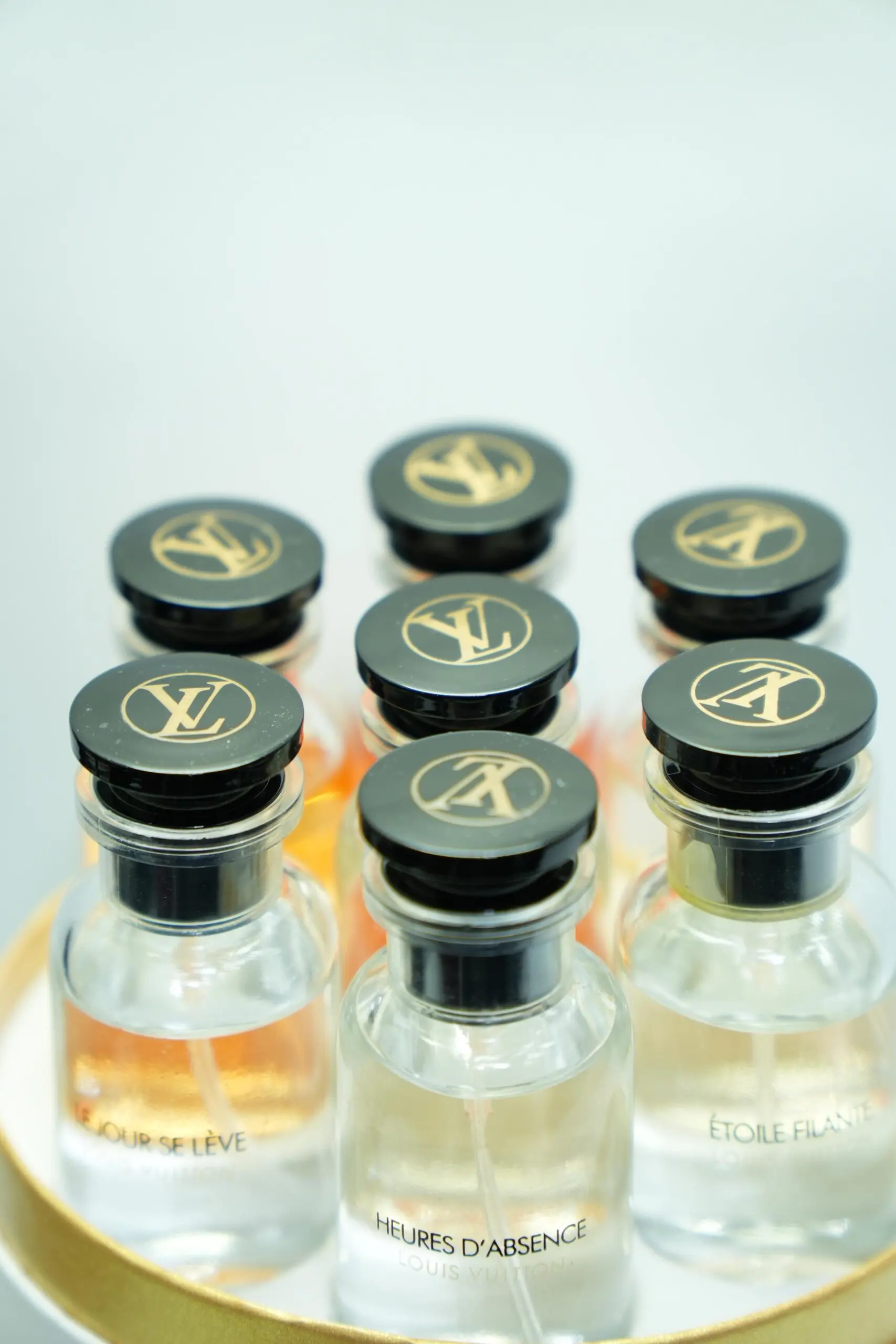 Estuche circular con siete botellas de perfume Louis Vuitton de lujo con atomizador, tapón negro y monograma dorado.