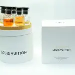 Set de miniaturas de perfumes Louis Vuitton en estuche cilíndrico blanco abierto con cinco botellas y caja de regalo al lado.