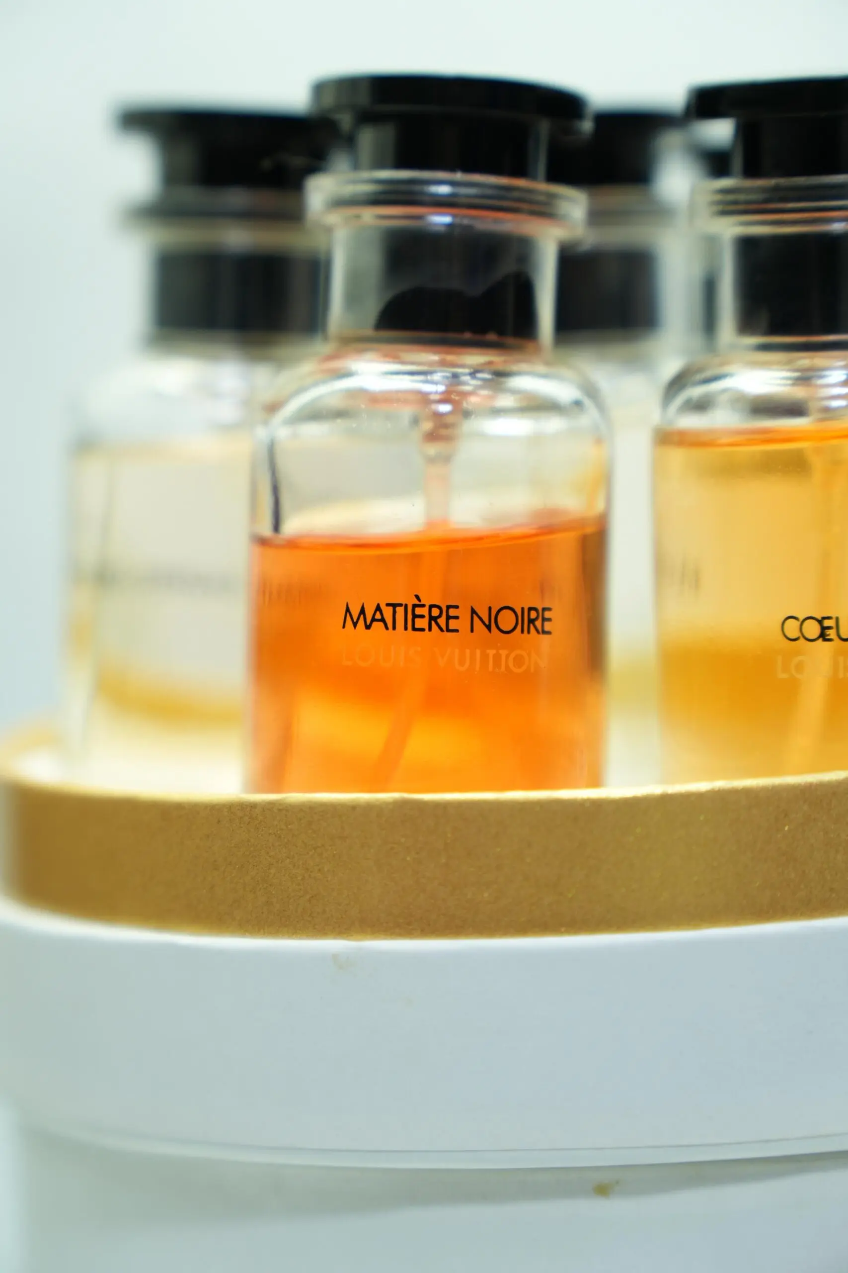 Set de perfumes Louis Vuitton en frascos de vidrio con líquido ámbar, organizados en estuche cilíndrico blanco y dorado