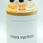 Estuche cilíndrico blanco y dorado de perfumes Louis Vuitton, que contiene varios frascos miniatura de vidrio con tapa negra y etiquetas visibles.