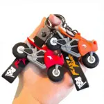 Set de tres llaveros tridimensionales de goma con diseño de motocicletas deportivas en colores rojo, naranja y negro, con detalles de banderas a cuadros.