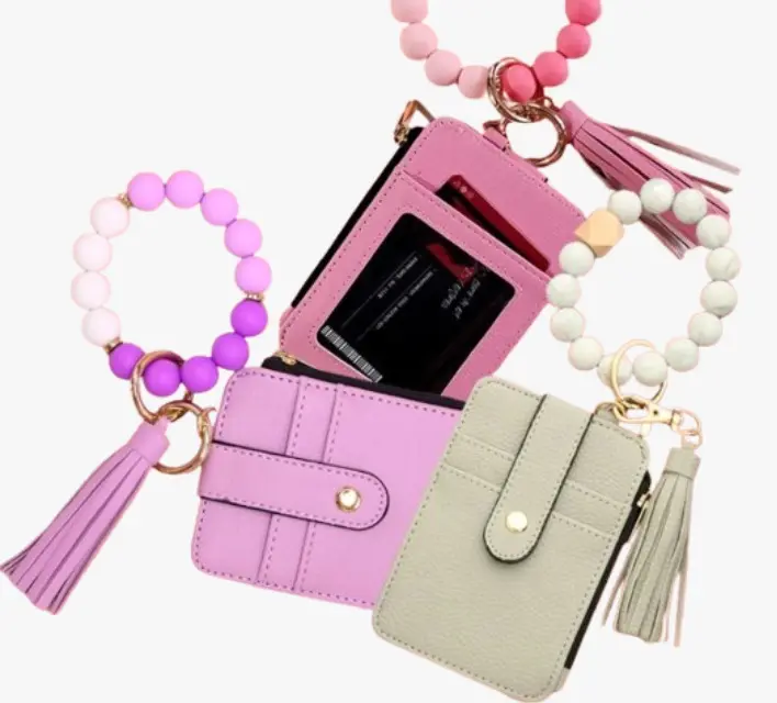 Tres carteras compactas con tarjetero, monedero y llavero de pulsera con cuentas de silicona y borlas decorativas en tonos rosa, lila y verde claro.