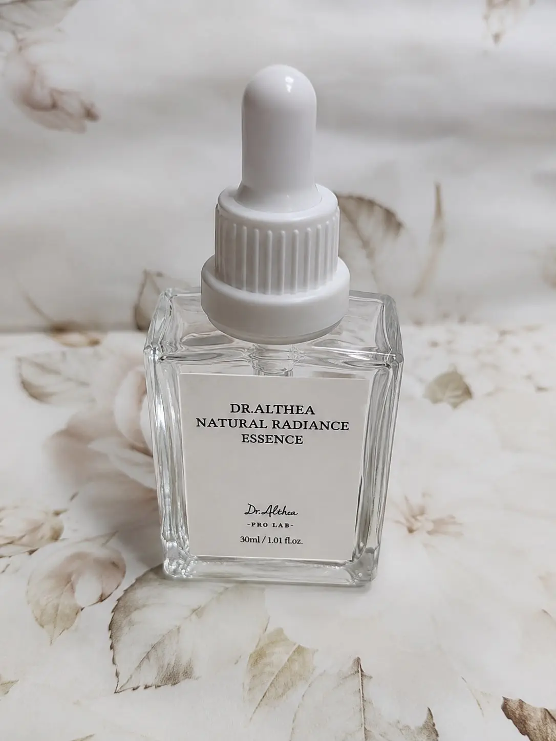 Esencia facial Dr. Althea Natural Radiance Essence de 30 ml en frasco de vidrio con gotero blanco sobre fondo de motivos florales.