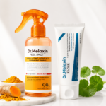 Set exfoliante Dr Melaxin con spray ámbar de cúrcuma y crema blanca Cica, junto a raíz de cúrcuma fresca y hojas verdes.