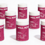 Siete frascos blancos con etiqueta fucsia y la marca Well Now, dispuestos en formación sobre superficie blanca para suplemento de cabello, piel y uñas.